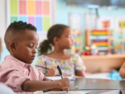 Male Primary Or Elementary School Student At Desk In Classroom